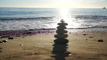 Balanced rock pyramid on pebbles beach, sunny day and clear sky at sunset. Golden sea bokeh on background. Selective focus, zen stones on sea beach, meditation, spa, harmony, calm, balance concept. video