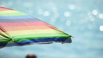 arcobaleno colorato spiaggia ombrelli o ombrelloni contro blu mare durante un' soleggiato giorno su un' spiaggia. simbolo di vacanze, relax, estate. colorato ombrelli a partire dal il sole In piedi su il spiaggia. lento movimento. video