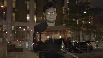 Jeune asiatique homme avec des lunettes en utilisant tablette écran ordinateur dans le ville à nuit video