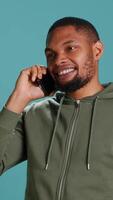 Vertical Man enjoying talking with friends in phone call using smartphone, isolated over studio background. Person conversating with mates during telephone call, catching up, camera A video