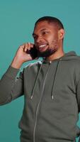 Vertical Man enjoying talking with friends in phone call using smartphone, isolated over studio background. Person conversating with mates during telephone call, catching up, camera B video