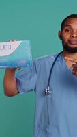Vertical Portrait of african american medic holding sleep deprivation medicine package for insomniacs, studio background. Healthcare specialist recommending tablets for patients with insomnia, camera B video
