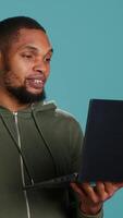 Vertical Joyful man having entertaining conversation with friends during teleconference meeting using laptop, studio background. Happy person having fun interacting with mates during online videocall, camera A video