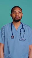 Vertical Portrait of jolly male caregiver standing with arms folded, isolated over studio backdrop. Cheerful person wearing protective clinical workwear to prevent spreading of diseases, camera B video