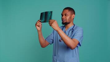 Male nurse analyzing radiology x ray scan to provide patient with diagnosis during medical exam, studio background. Practitioner doing body examination, scanning radiography, camera B video