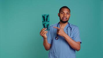 Healthcare professional informing patient of radiology x ray scan results, studio backdrop. African american doctor presenting radiography and providing injury treatment, camera B video