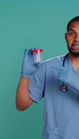 Vertical Portrait of male nurse holding blood sample container, doing medical investigation for sick patient, isolated over studio background. Hospital staff member with microbiology test tube, camera B video