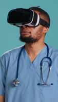 verticale infirmière portant virtuel réalité casque à distance en fonctionnement patient. soins de santé spécialiste en utilisant haute technologie futuriste moderne médical vr gadget, isolé plus de bleu studio arrière-plan, caméra une video