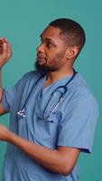 Vertical Male nurse pointing finger towards empty space doing advertising, talking with audience. Healthcare worker doing presentation, showing copy text, studio backdrop, camera B video