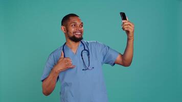 Male nurse using mobile phone to take selfies during hospital job shift break. Healthcare worker using smartphone to take pictures of himself, isolated over studio background, camera B video