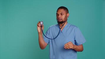 Male nurse using stethoscope on patient during medical exam, hearing heartbeat, isolated over studio background. Healthcare worker using clinic equipment to check for cardiac issues, camera B video