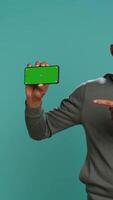 Vertical Portrait of upbeat content creator doing influencer marketing using green screen mobile phone. Cheerful person holding chroma key cellphone device, isolated over studio backdrop, camera B video