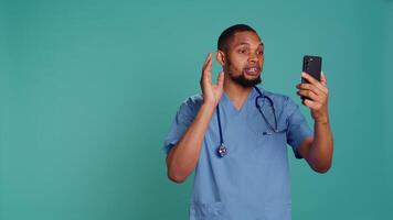 Male nurse in videocall meeting using mobile phone, greeting people. Healthcare expert in online telemedicine call with patients using smartphone, isolated over studio background, camera B video