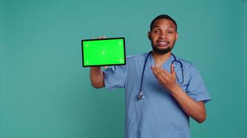 ritratto di africano americano maschio infermiera mostrando medico Istruzioni su isolato schermo tavoletta. assistenza sanitaria lavoratore Tenere modello digitale dispositivo, studio sfondo, telecamera B video