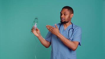 Male nurse doing medical instruction on how to use handheld nebulizer used for delivering aerosols based medicines. Medic presents inhalation device for lung diseases like pneumonia, camera B video