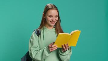 adolescenziale donna con libro nel mani mostrando apprezzamento per letteratura, isolato al di sopra di studio sfondo. giovane lettura appassionato Tenere romanzo, godendo lettura passatempo, telecamera un' video