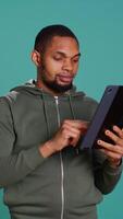 Vertical Upbeat man adding payment method on online website using tablet. Person thrilled to do internet shopping using device, typing debit card data, isolated over studio background, camera B video