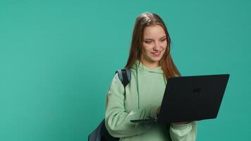 Radiant woman opening laptop to prepare for school exam, isolated over blue studio background. Upbeat student using notebook to prepare for university classes, studio backdrop, camera A video
