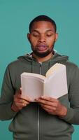 Vertical Man reading book aloud, narrating story for audience. Person enjoying literature novel, reciting from pages, entertaining spectators, isolated over studio background, camera B video