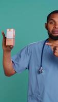 Vertical Portrait of nurse holding spf50 sunscreen product, doing recommendation to patients, isolated over studio background. Healthcare expert urging people to use UV solar protection, camera B video