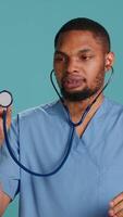Vertical Male nurse using stethoscope on patient during medical exam, hearing heartbeat, isolated over studio background. Healthcare worker using clinic equipment to check for cardiac issues, camera A video