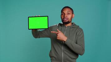 Tech content creator holding isolated screen tablet, doing promotion, talking with audience. Man pointing towards chroma key digital device, doing advertising, studio backdrop, camera B video