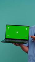 Vertical Portrait of african american medic in protective medical uniform using green screen laptop. Healthcare specialist doing presentation using mockup notebook, showing patient treatment plan, camera B video