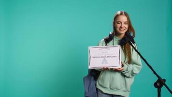 Happy student holding diploma talking in microphone, addressing audience, holding speech, studio background. Inspiring teenager using mic to share feeling during graduation ceremony, camera B video