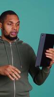 Vertical Angry man fighting with friend during videocall on tablet, isolated over studio background. Rude person in disagreement with mate, swearing and pointing finger in teleconference meeting, camera B video