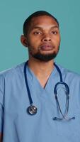 Vertical Portrait of jolly male caregiver standing with arms folded, isolated over studio backdrop. Cheerful person wearing protective clinical workwear to prevent spreading of diseases, camera A video