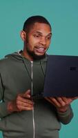 Vertical Joyful man having entertaining conversation with friends during teleconference meeting using laptop, studio background. Happy person having fun interacting with mates during online videocall, camera B video