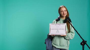 Overjoyed student celebrating achievement, holding diploma, using microphone to do speech, studio background. Woman using mic to share wisdom with colleagues after finishing school, camera B video