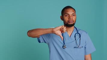 Upset nurse showing thumbs down signs while at work, isolated over blue studio background. Disappointed healthcare professional doing frenetic disapproval gestures, camera A video