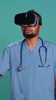 Vertical African american doctor wearing virtual reality goggles, remotely operating patient. Hospital staff member using high tech medical vr device, isolated over studio backdrop, camera B video