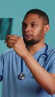 Vertical Male nurse analyzing radiology x ray scan to provide patient with diagnosis during medical exam, studio background. Practitioner doing body examination, scanning radiography, camera A video