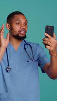 Vertical Male nurse in videocall meeting using mobile phone, greeting people. Healthcare expert in online telemedicine call with patients using smartphone, isolated over studio background, camera B video