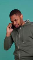 Vertical Irked african american man fighting with friends during telephone call, isolated over studio background. Outraged person arguing with mates during conversation on mobile phone, camera B video