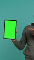 Vertical Joyous african american man holding isolated screen laptop, doing recommendation. Upbeat person pointing towards chroma key device, giving positive feedback, studio background, camera B video