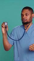 Vertical Male nurse using stethoscope on patient during medical exam, hearing heartbeat, isolated over studio background. Healthcare worker using clinic equipment to check for cardiac issues, camera B video