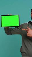 Vertical Tech content creator holding isolated screen tablet, doing promotion, talking with audience. Man pointing towards chroma key digital device, doing advertising, studio backdrop, camera B video