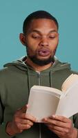 Vertical Man reading book aloud, narrating story for audience. Person enjoying literature novel, reciting from pages, entertaining spectators, isolated over studio background, camera A video