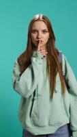 Vertical Stern woman doing shushing hand gesturing, irritated by noise, having negative mood. Girl placing finger on lips, doing quiet sign gesture, isolated over studio background, camera B video