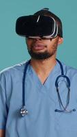 vertikal afrikansk amerikan läkare bär virtuell verklighet glasögon, avlägset rörelse patient. sjukhus personal medlem använder sig av hög tech medicinsk vr enhet, isolerat över studio bakgrund, kamera en video