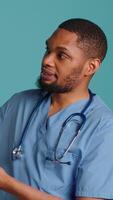 Vertical Male nurse pointing finger towards empty space doing advertising, talking with audience. Healthcare worker doing presentation, showing copy text, studio backdrop, camera A video