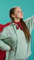 Vertical Portrait of jolly girl wearing superhero costume for Halloween, isolated over studio backdrop. Radiant teenage person dressed as comic book hero for event, showing courage and strength, camera B video