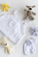 Set of white clothes and accessories for newborn baby. Knitted toys, knitted romper, socks on white wooden background. photo