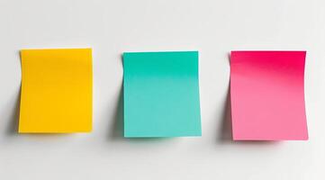 Three colourful post-it sticky notes are hanging on a white wall photo