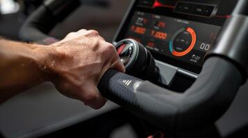 A closeup of a hand gripping onto the handlebars of an advanced indoor cycling bike with a digital display showing realtime metrics such as cadence and resistance level photo