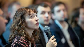 A panelist confidently speaks into a microphone as they answer a thoughtprovoking question. The audience looks on with some nodding in agreement and others deep in thought photo