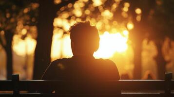 The silhouette of a man sitting on a park bench lost in thought as the sun sets behind him photo